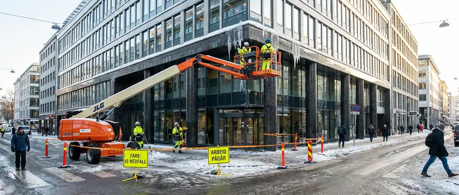 Et oversiktsbilde som viser en travel gate i Oslo med tydelige varselskilt og en lift som fjerner istapper fra et høyt næringsbygg
